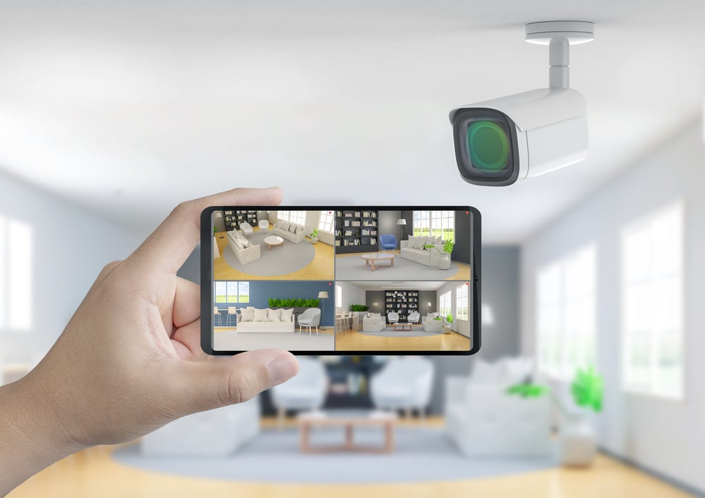 Smartphone displaying a home security camera feed in a bright living room, highlighting remote monitoring features